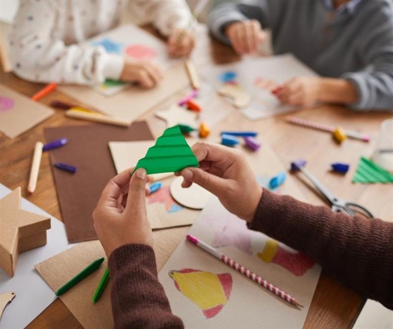 children sit and make a paper christmas tree
