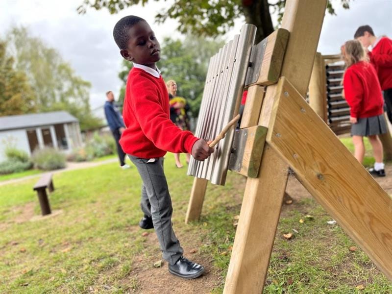 a child stands and plays a tune on the freestanding chimes
