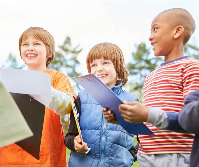 Three children are holding clipboards and paper whilst smiling and laughing.
