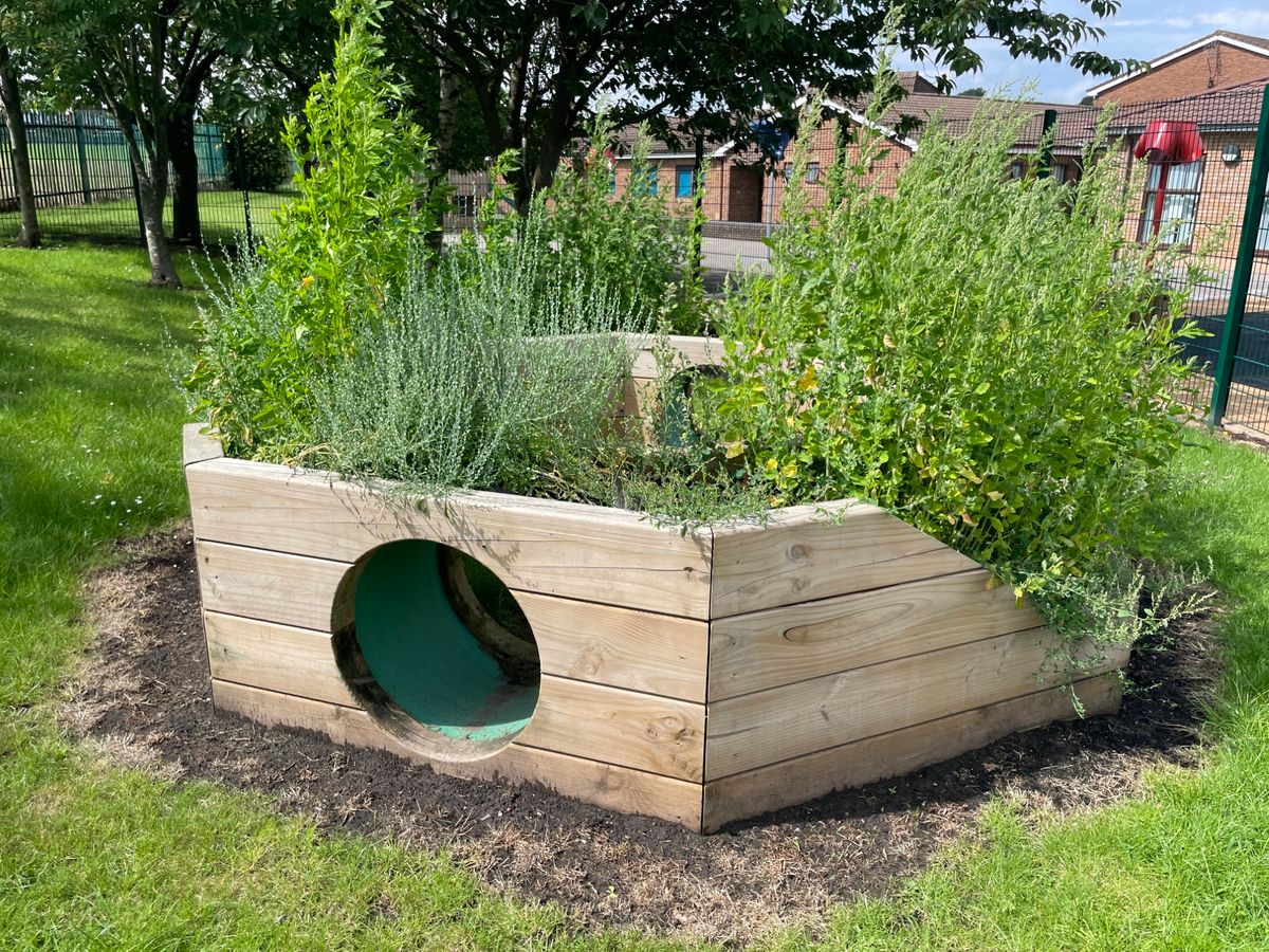 A picture of our Immersive Planter product placed on a school field. The angle of the photo shows the tunnel entrance.