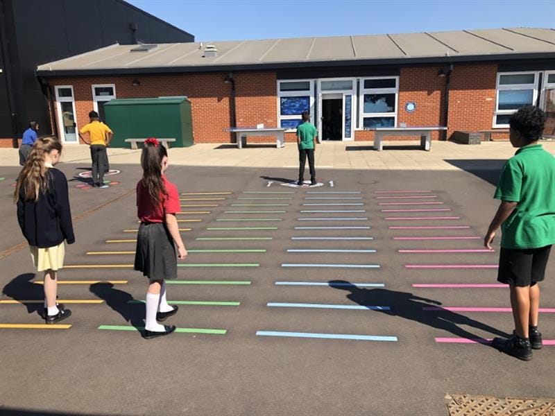 Four children are playing the game "Mr Wolf". One of the children is Mr Wolf and is standing with his back towards his camera, quite far away. The other three kids are ready to move closer to him as they are closer to the camera.