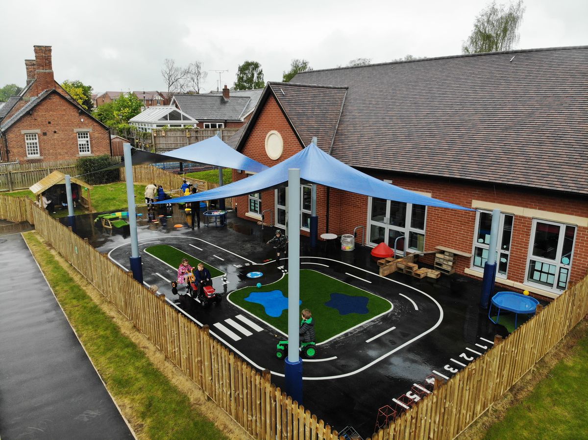 A drone shot showing a roadway marking done by Pentagon Play. The road has 4 children driving little cars on it, with two canopies covering the area.
