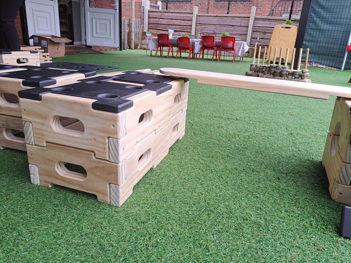 A close up photo of the Accoya material being used to produce the Play Builder set. The wood is light in colour. Two wooden blocks are put on top of each other and have one end of a plank placed on it. The other end of the plank is connecting to another block.