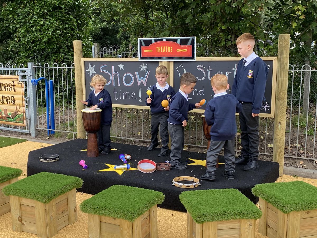 Five children are stood on an outdoor performance stage whilst holding on to some musical instruments.