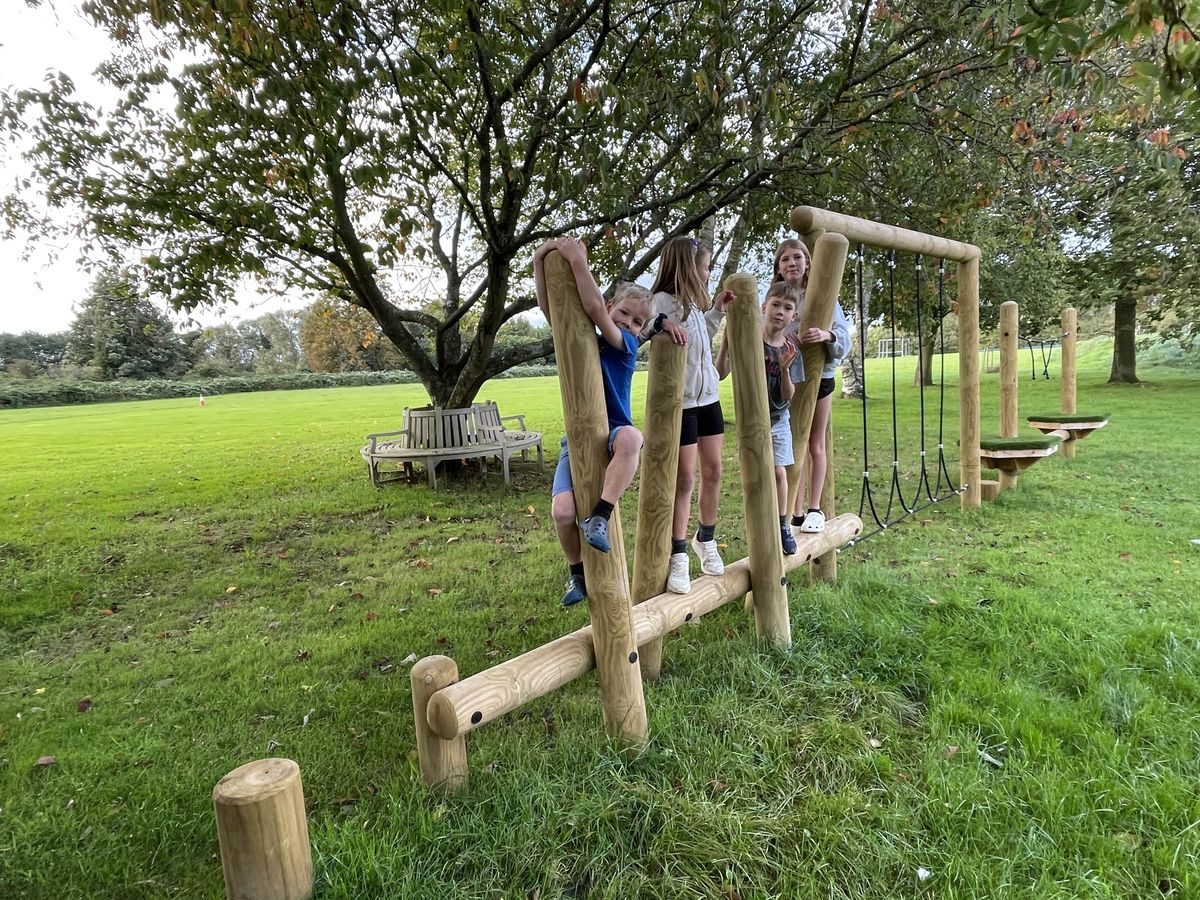 A group of children are climbing across a trim trail and are looking into the camera and smiling.