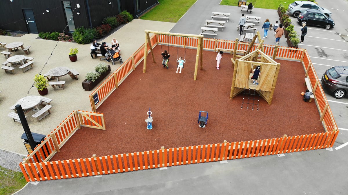 A birdseye shot showcasing a simple playground that has been installed at a holiday park, beside a seating area.