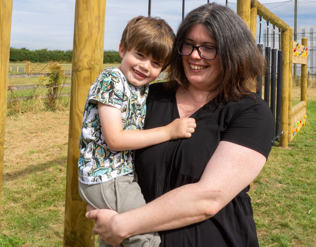 A mother and son are stood beside an active trim trail installed by Pentagon Play. The mother and child are looking at the camera and smiling.