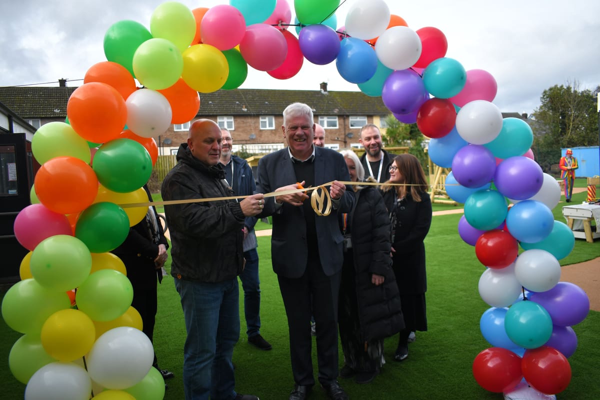 A group of stakeholders are posing underneath a balloon arch as they cut a ribbon to open their new playground.