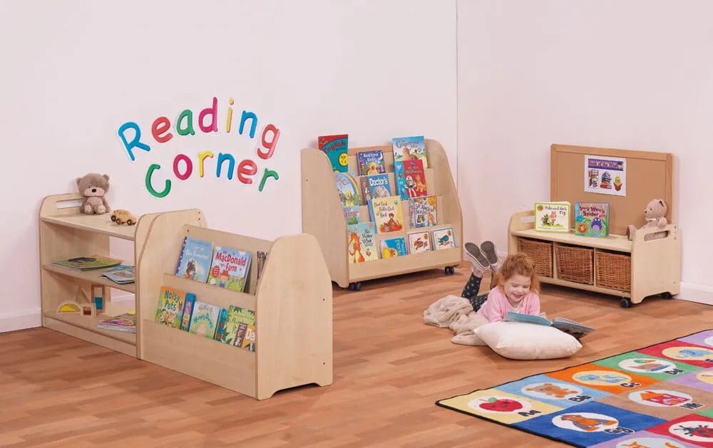 A little girl is lay on some cushions that have been placed on the floor. She is reading a book as a variety of book shelves surround her.