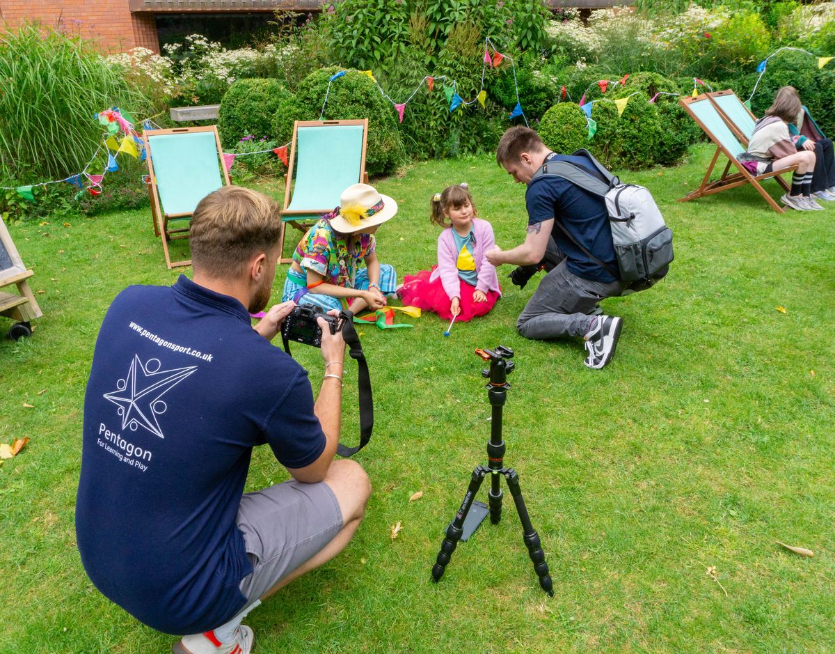 Two Pentagon Play employees are taking pictures of a mum and her daughter playing outside.