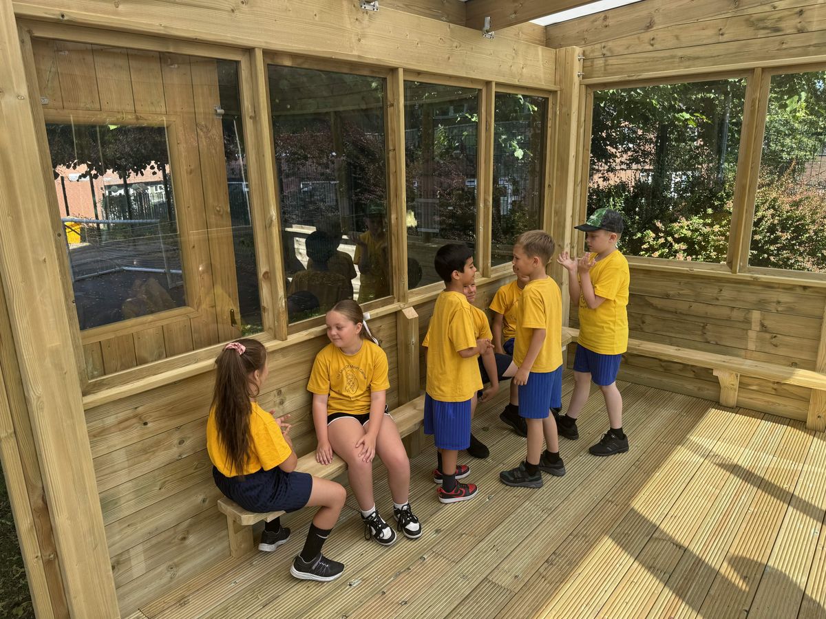 A group of KS2 children are sat within an outdoor classroom, talking with each other.