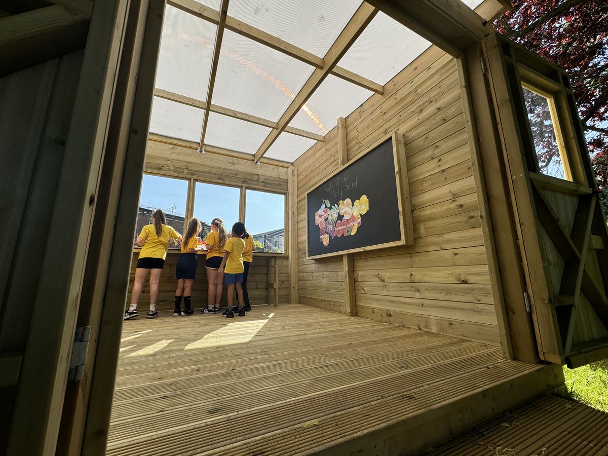 The inside of an outdoor classroom with a blackboard installed on the back wall with a variety of fruits and veg drawn on it.