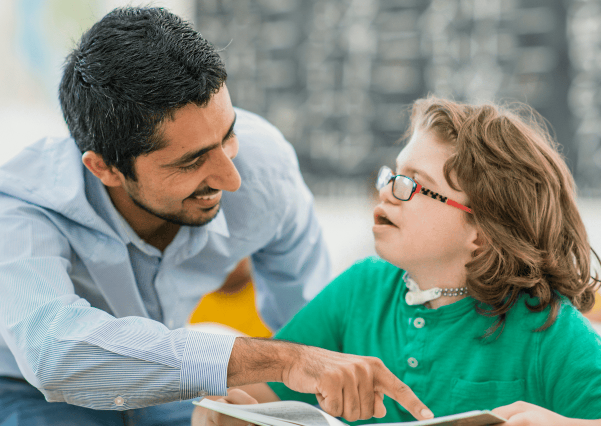 A teaching assistant is showing an SEN girl something on her worksheet.