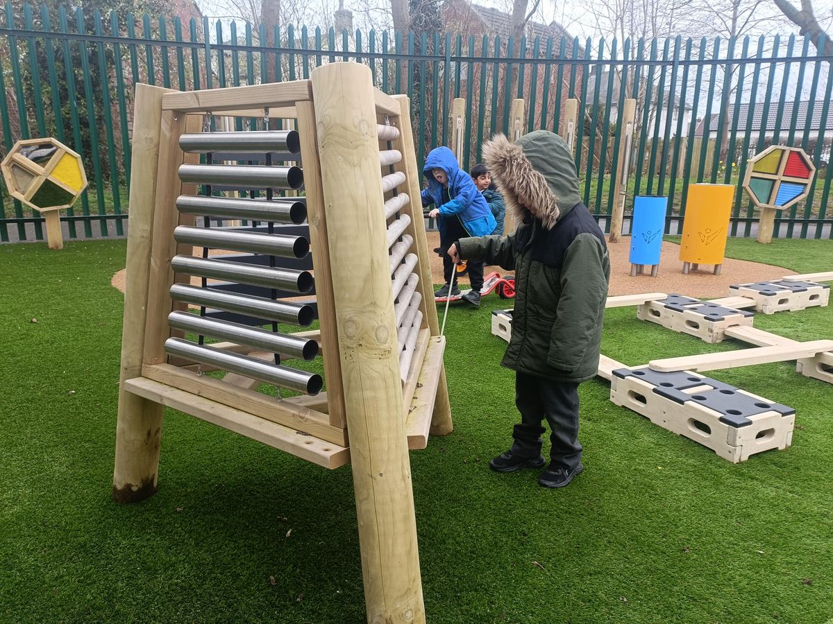 A little boy is stood beside the freestanding Xylophone and is holding a beater in his hands.