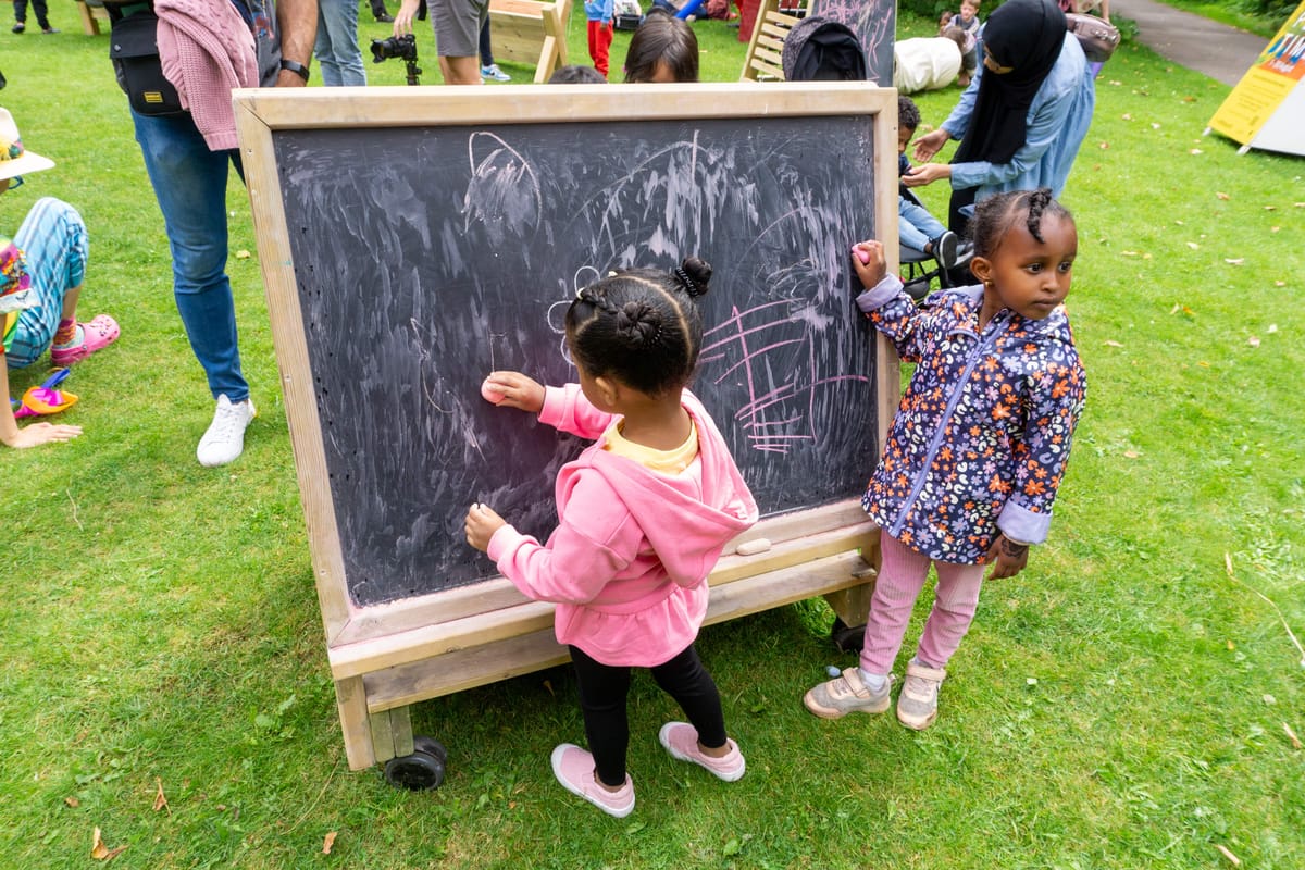 Two little girls are drawing on a movable chalkboard with different colour chalk.