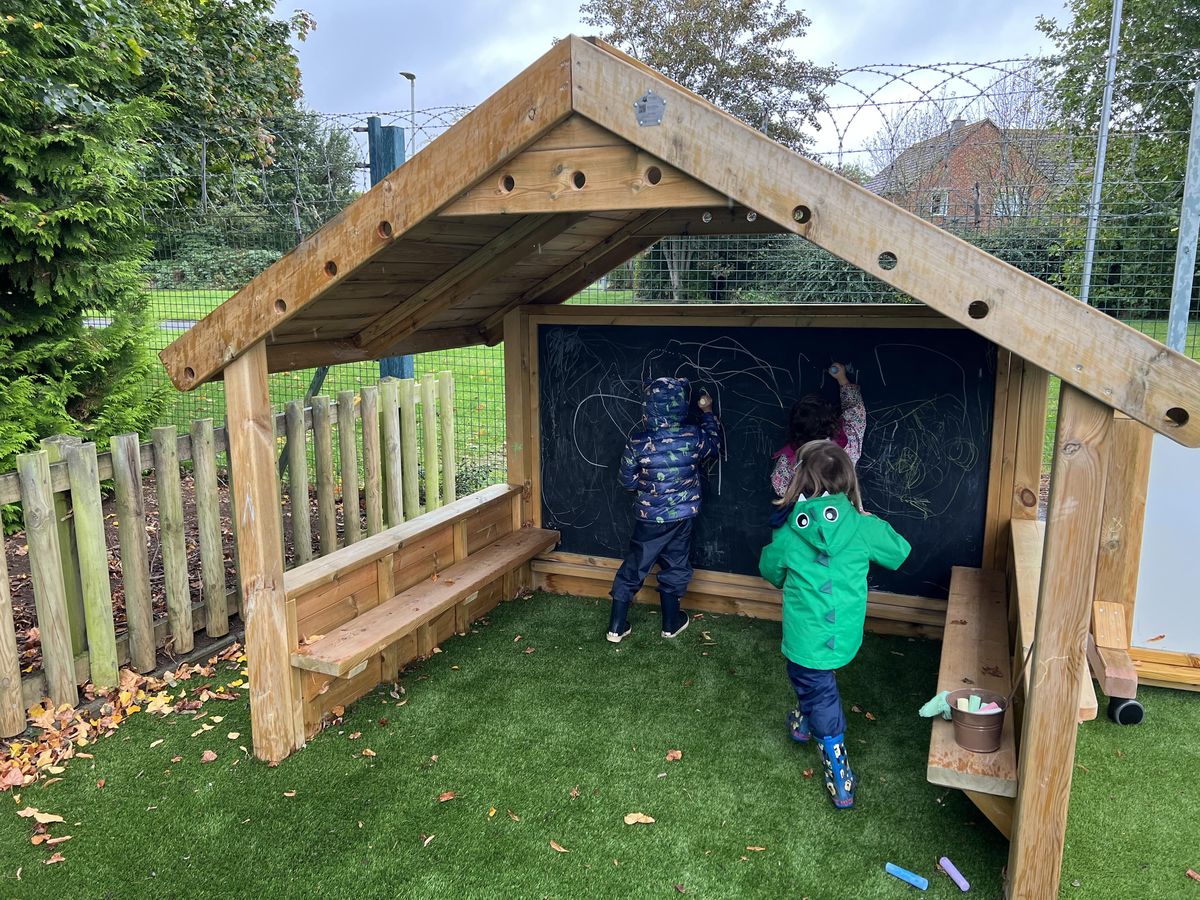 Two children are playing in a Giant Playhouse and are drawing on the chalkboard on the back.