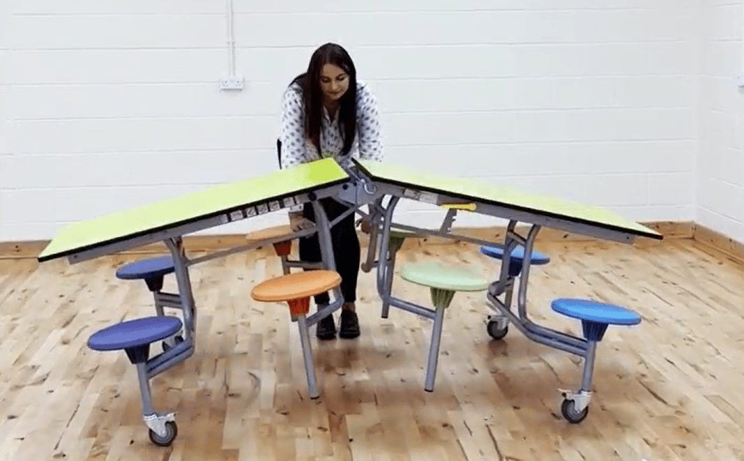 A woman is unfolding a school dining table, showcasing how easy it is to manoeuvre them.