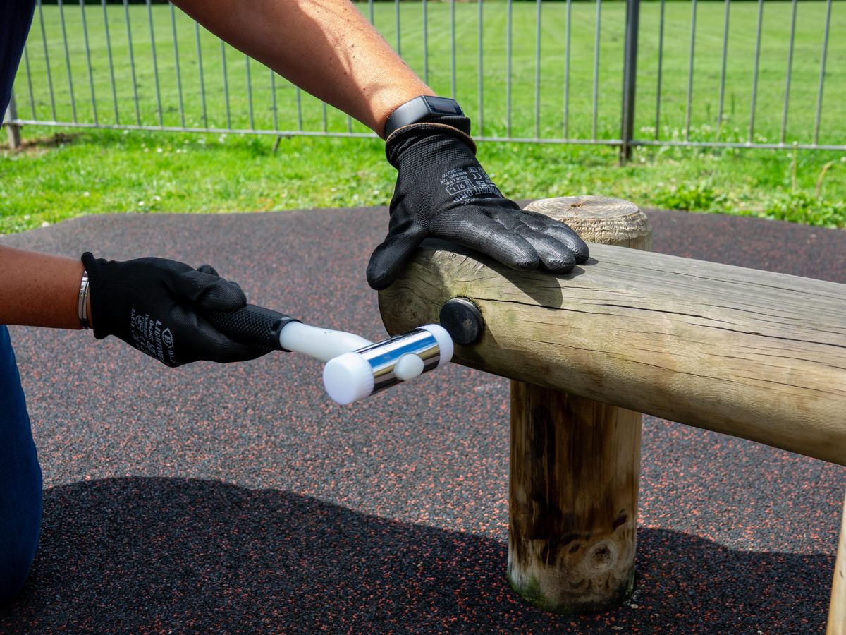 A man is hammering a bolt cap onto a piece of play equipment.