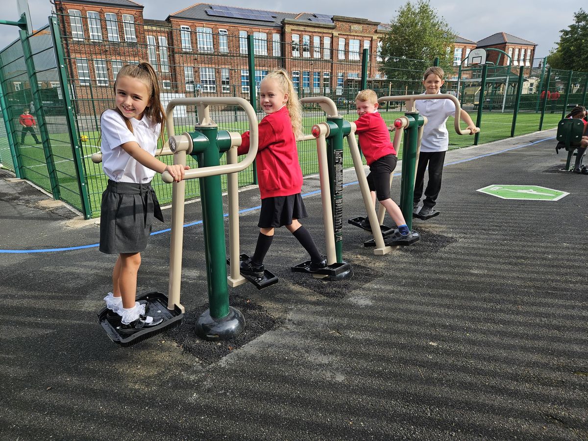 Four children are standing on outdoor gym equipment as they all look towards the camera and smile.