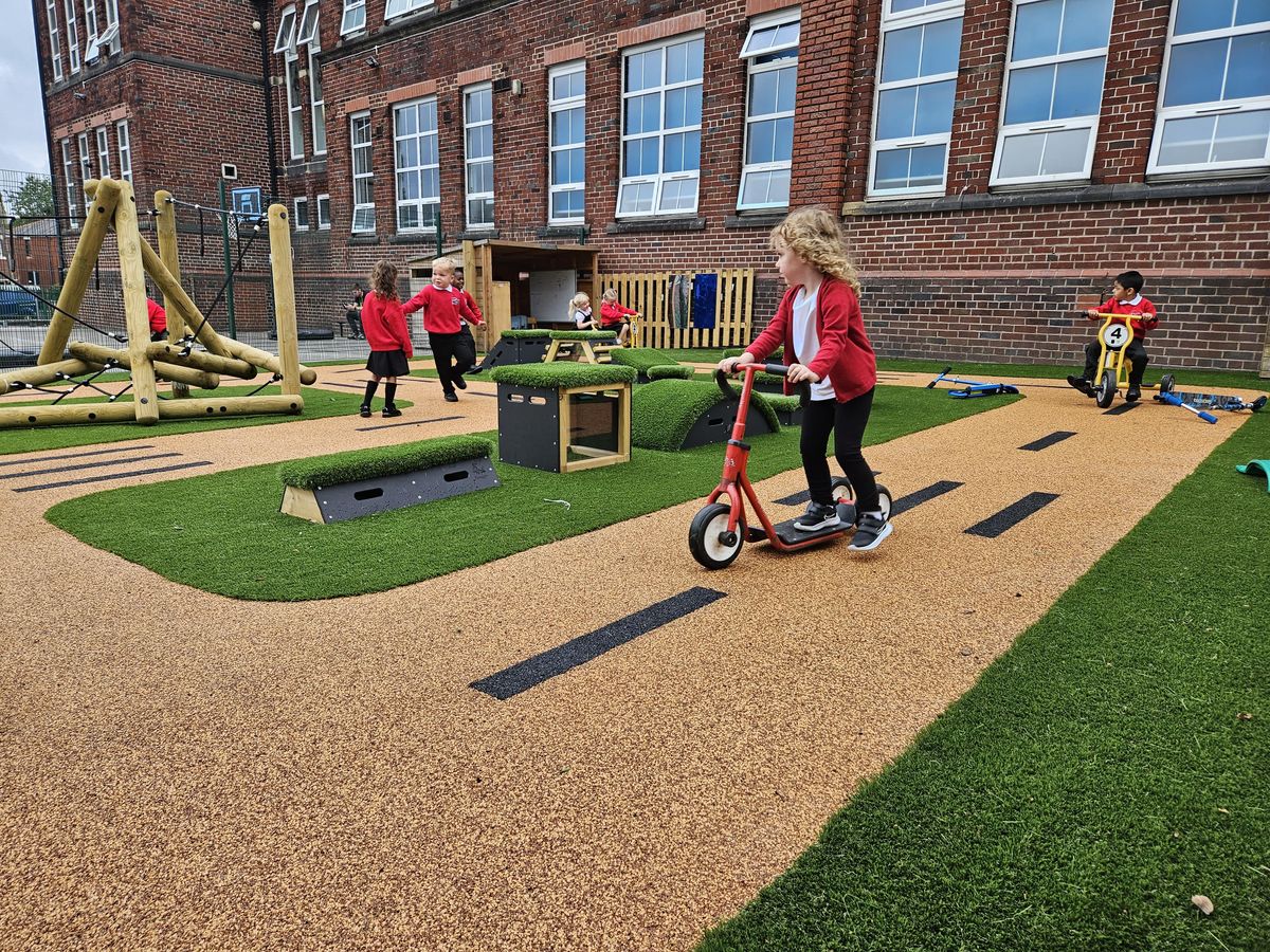 A little girl is on a scooter and is rolling on a wetpour road as she looks around.
