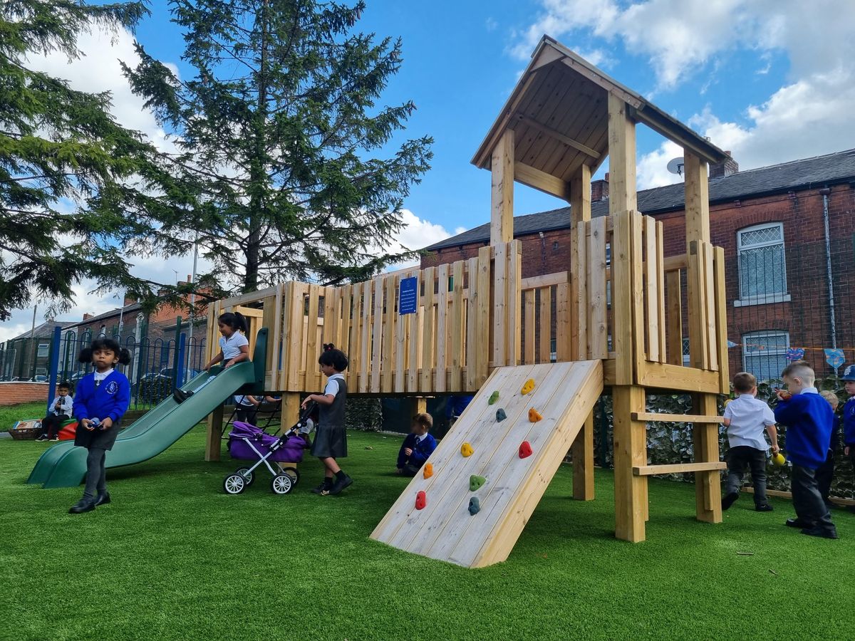 A giant play tower on an artificial grass surface, with a class of primary school children exploring the structure.