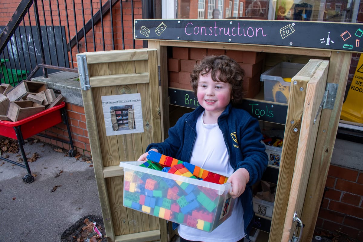 A little child is taking a box of building bricks out of the Acorn Storage Unit and is smiling at the camera.