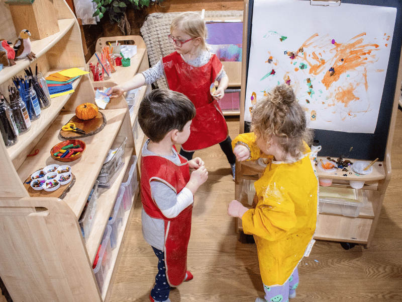 Three children are stood in the middle of a Millhouse Creative Zone as they look around for materials and art supplies.