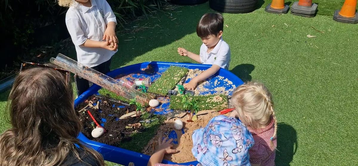 A small group of kids are adding a variety of sensory materials to the tuff table, creating distinctive zones within the tray.