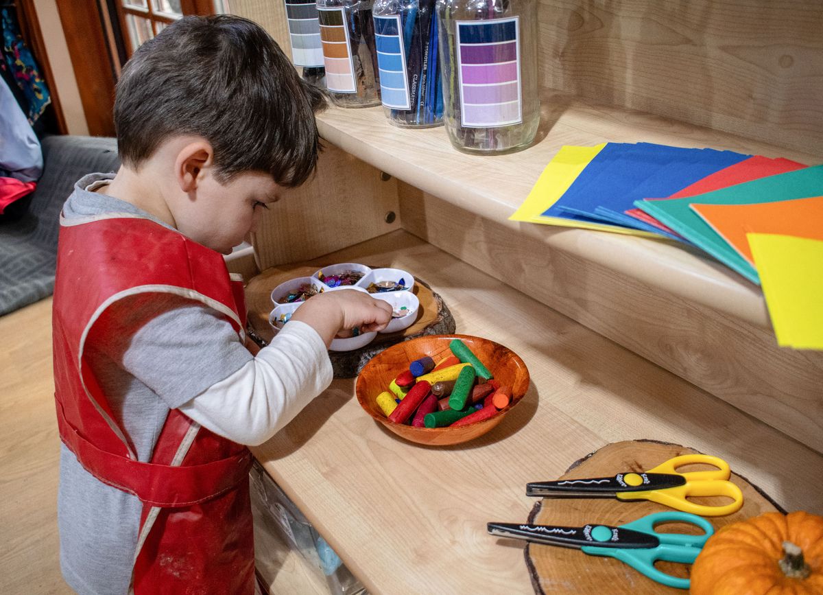 A little boy is picking up some arts & crafts bits to create a piece of art.