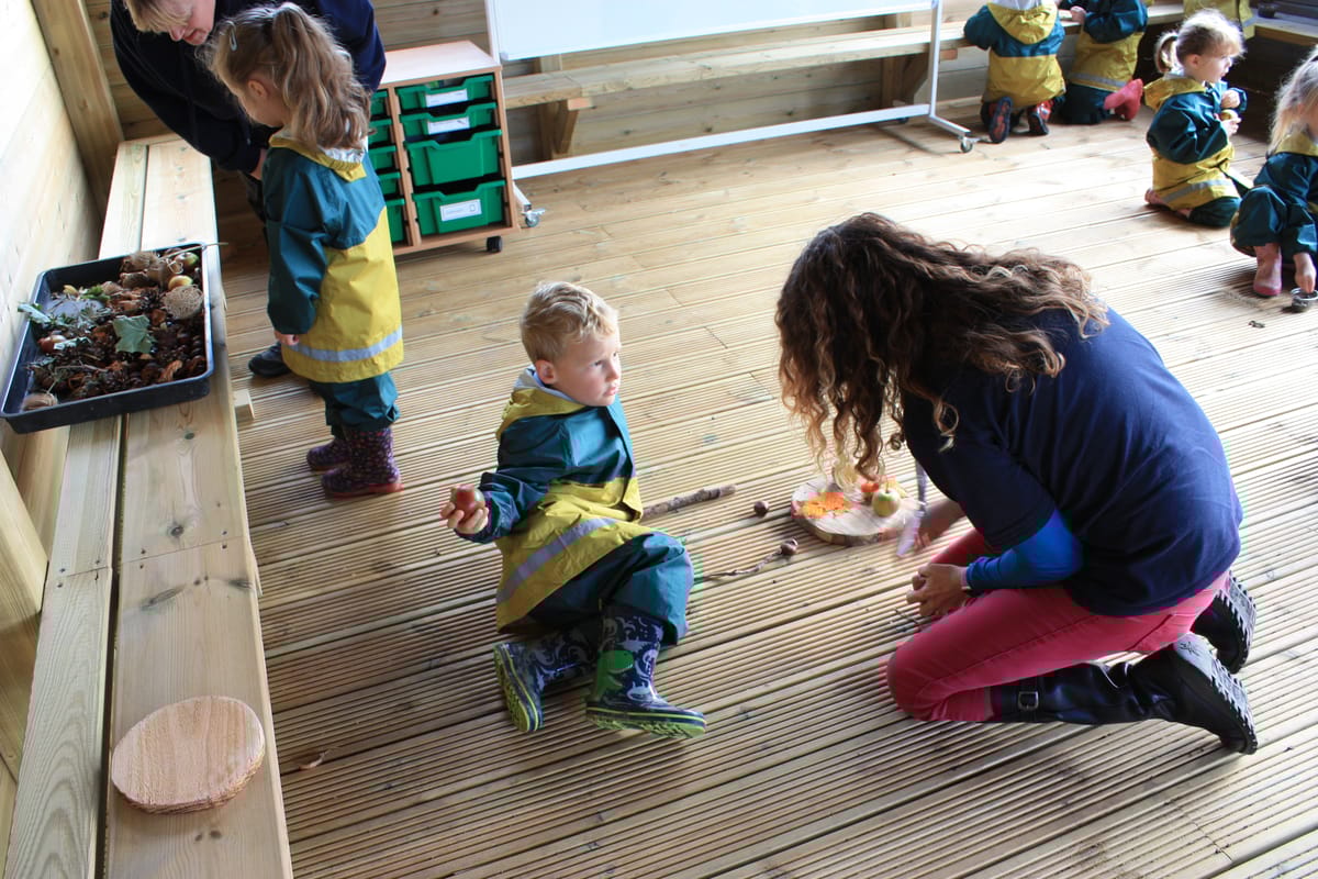 A little boy is playing with a teacher with natural materials in an outdoor classroom.