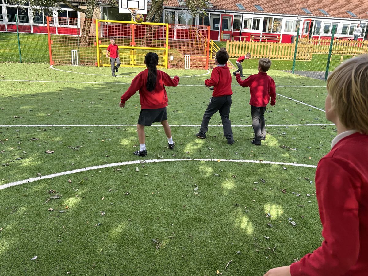 A small group of children are playing on an artificial grass MUGA, which has colourful fencing going around the border.