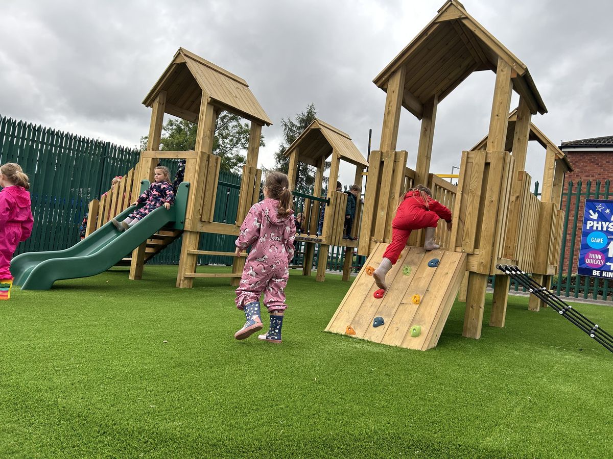 A play tower that has been installed on artificial grass, as toddlers climb the structure.
