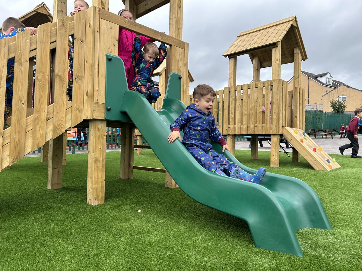 A group of children are going down a slide that is attached to a play tower, smiling.
