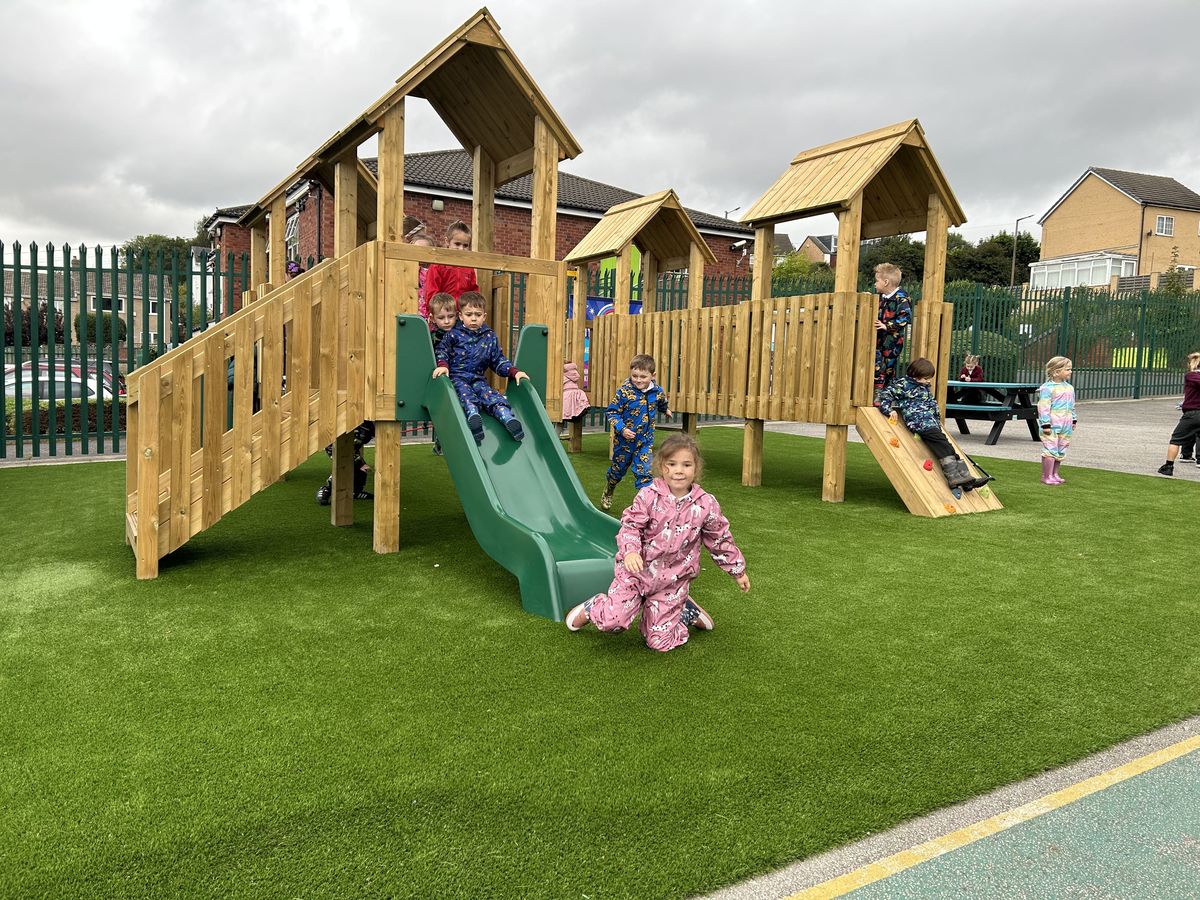 A play tower installed on top of an artificial grass surface, with EYFS children on it.