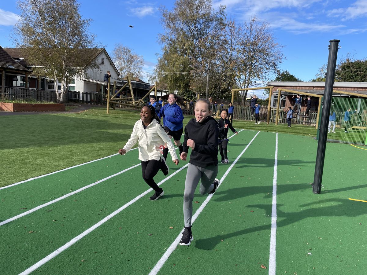 A group of 4 children are hopping on an artificial grass track as they make their way towards the camera.