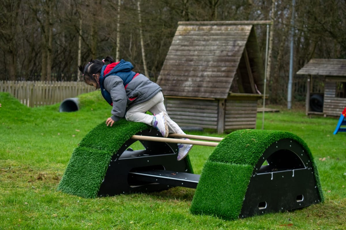 A little girl is climbing over the block at the end of the Rockies. They have just come off the wobble board.