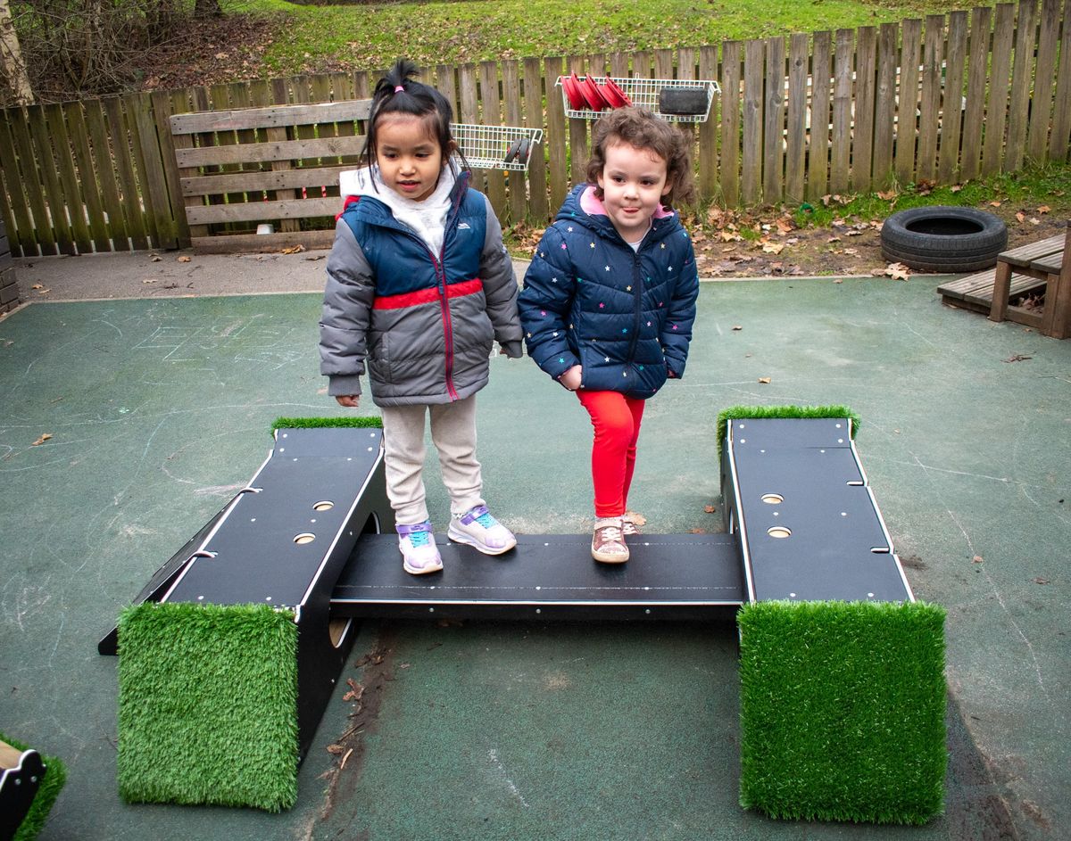 2 girls are looking at the camera as they stand on the wobble board included in the Rockies.