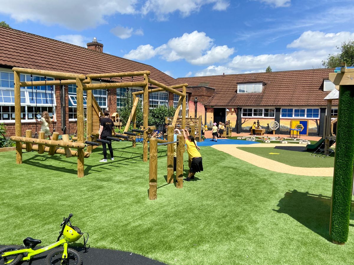 A large playground with children playing on it. A variety of different play equipment can be seen across the area, with different safety surfacing.