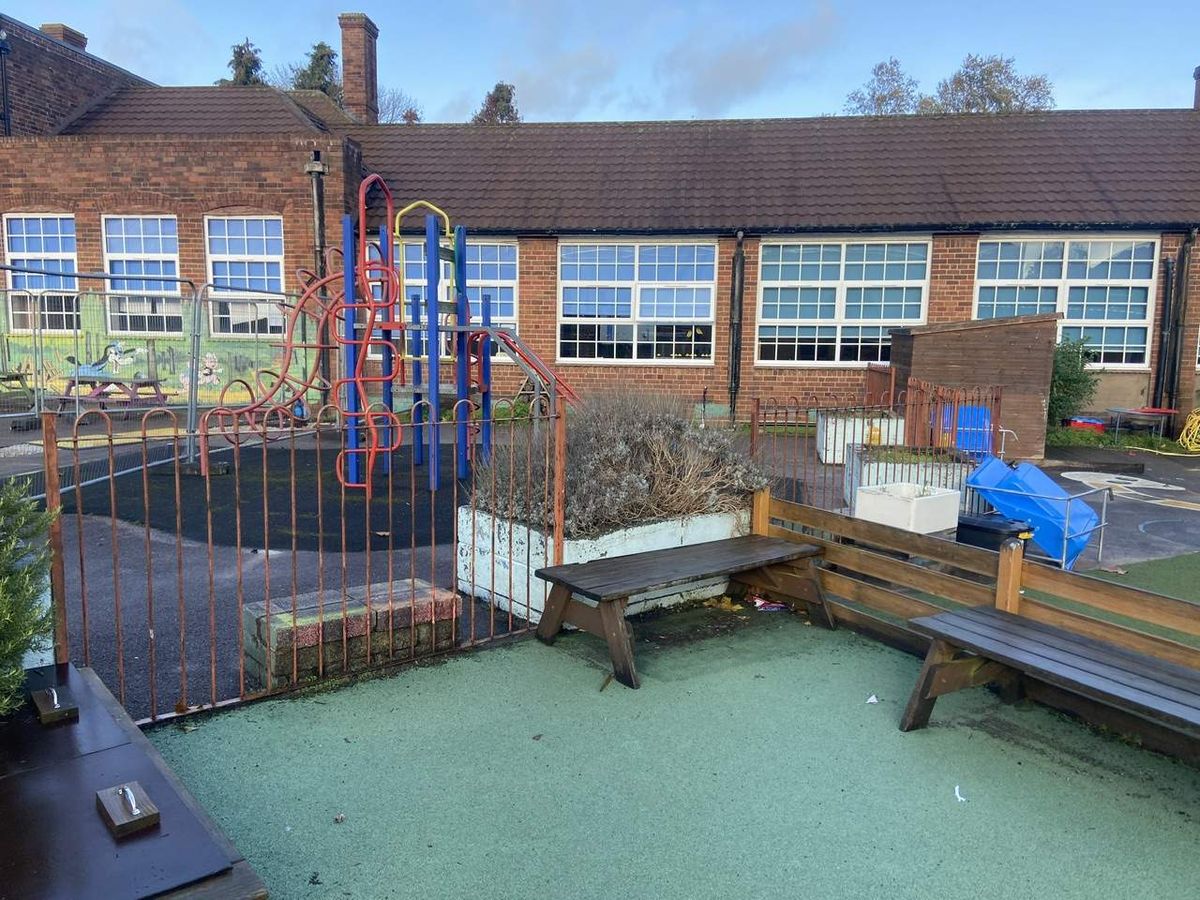 An old playground that has rusted playground equipment and fencing, with faded wetpour surfacing.