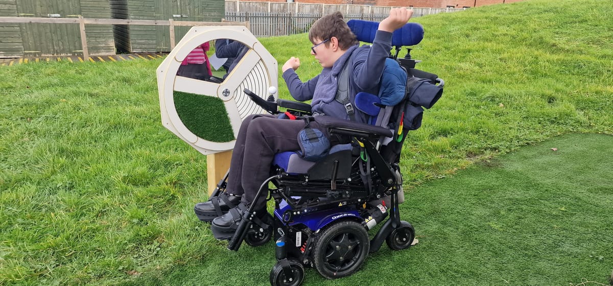 A boy in a wheel chair is spinning a Sensory Spinner installed on grass.