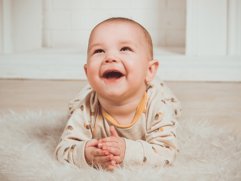 A baby looking above the camera and laughing. The baby is lay on it's stomach.