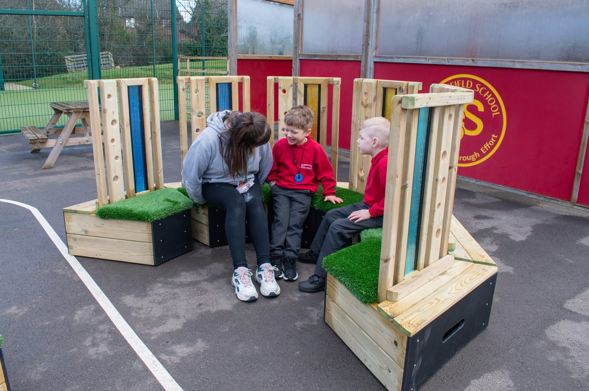 A teaching assistant is sat with two SEN boys on the Sensory Seating Circle.