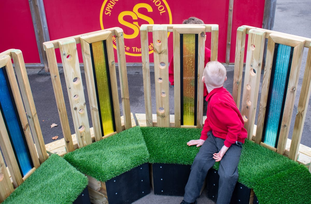 A little boy is sat on a Sensory Seating Circle as he looks through the coloured plastic to see another child.