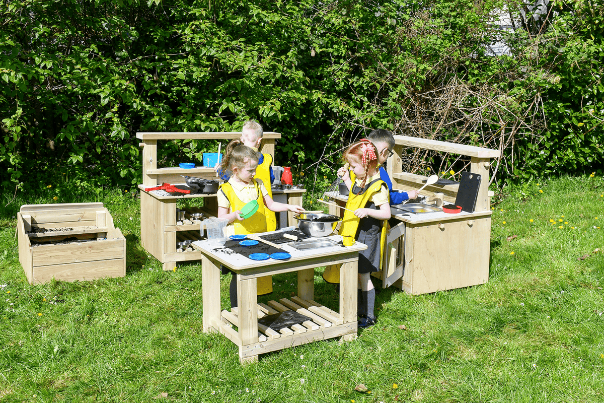 Four children are playing with a Mud Kitchen set, with each child taking on a different responsibility and focusing on preparing a meal.