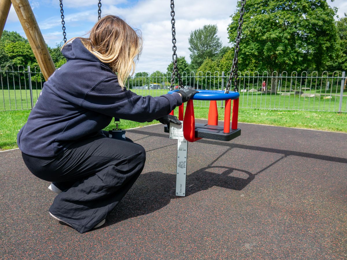 A playground inspector is checking the critical fall height of a swing.