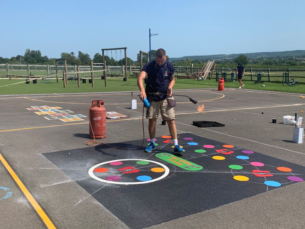 A Pentagon Play marking installer is carrying a torch and is burning the graphics to the playground.
