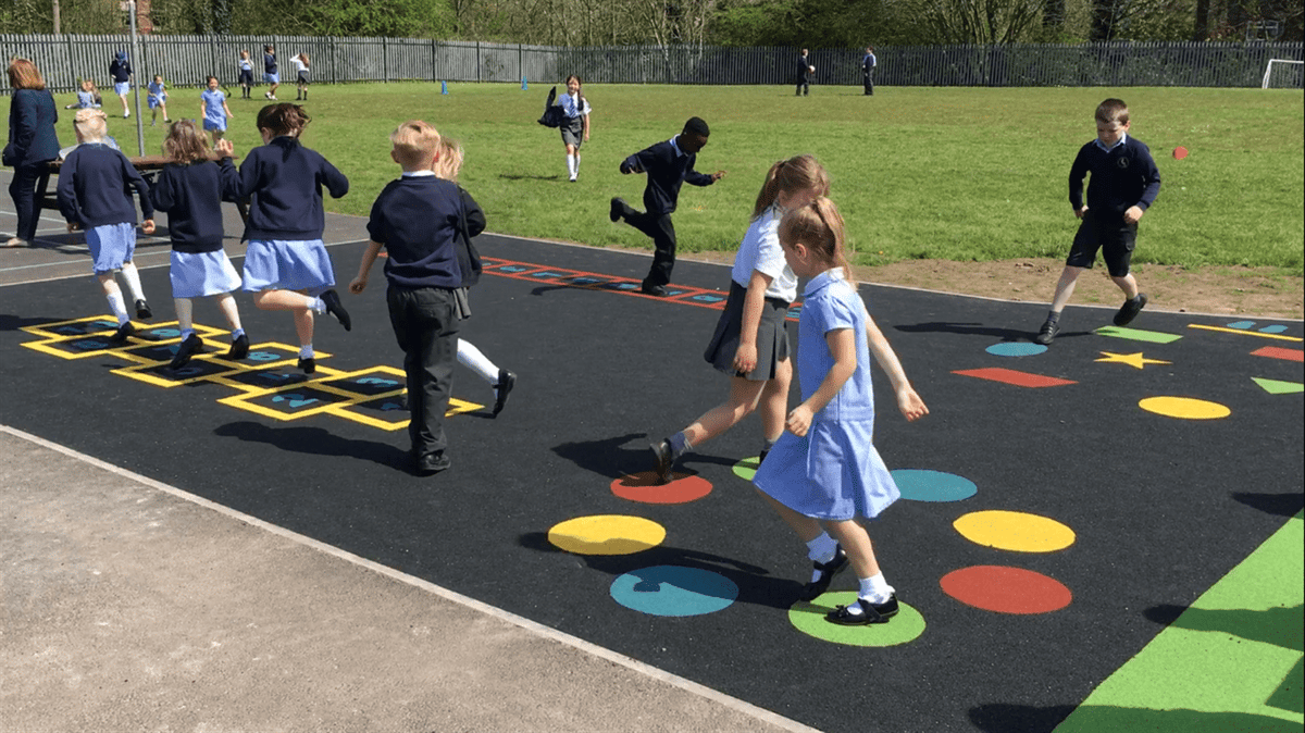 A group of school children are playing on a playground that has a variety of playground markings on it.