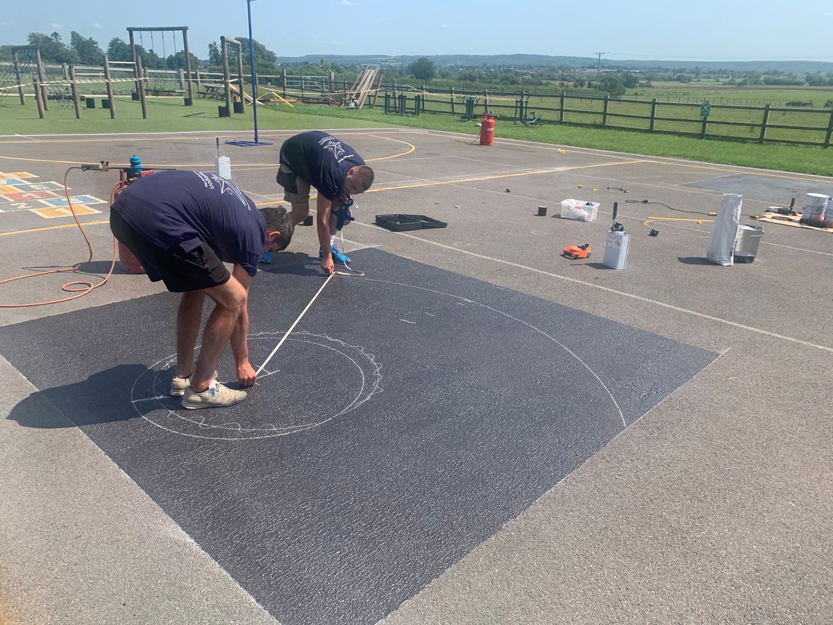 Two thermoplastic graphic installers are planning an area out for a new playground marking to be installed on.