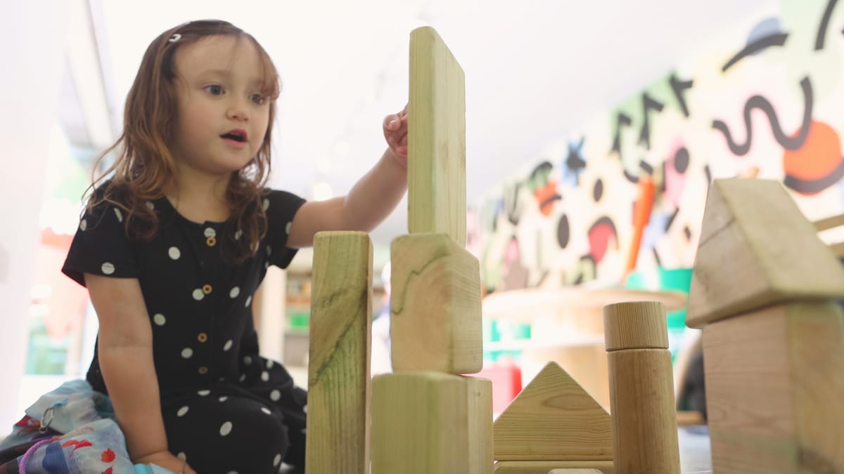 A little girl is stacking blocks as she looks amazed, having a lightbulb moment.