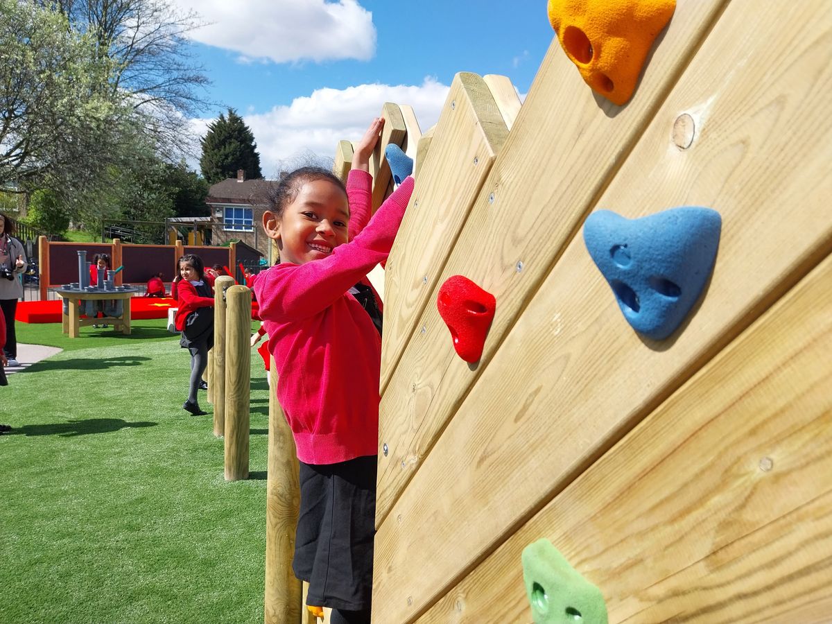 A girl is climbing across a Climbing Wall and is smiling at the camera.